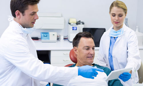 Two dentists and a patient looking at treatment information on a tablet